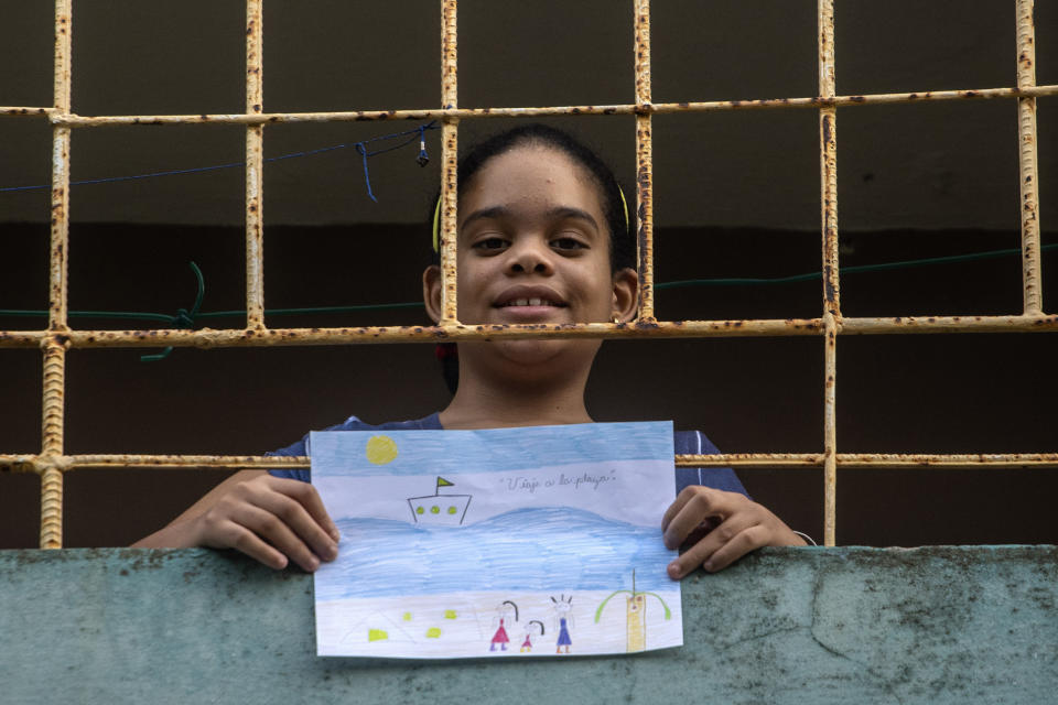 En esta imagen, tomada el 8 de mayo de 2020, Ana Laura Ramírez Lavandero, de 10 años, sostiene un dibujo en el que expresa su deseo de viajar a la playa, desde el balcón de su casa en La Habana, Cuba. El único momento en que ha podido salir de su casa en casi dos meses fue para ir de emergencia al dentista. Las escuelas están cerradas, y como muchas personas en Cuba no tienen internet, el Ministerio de Educación transmite las lecciones por la televisión estatal. (AP Foto/Ramón Espinosa )