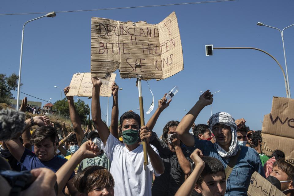 Migrants take part in a rally as the banner reads in German "Germany Please Help Us" near Mytilene town, on the northeastern island of Lesbos, Greece, Friday, Sept. 11, 2020. Thousands of protesting refugees and migrants left homeless on the Greek island of Lesbos after fires destroyed the notoriously overcrowded Moria camp have gathered on a road leading to the island's main town, demanding to be allowed to leave. (AP Photo/Petros Giannakouris)