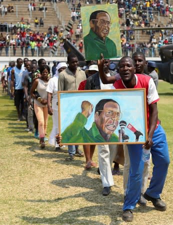 Mourners hold paintings with the face of former Zimbabwean president Robert Mugabe, as they queue to pay their last respects as he lies in state at the at Rufaro stadium, in Mbare