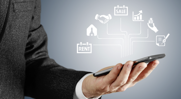 An image of a man holding a phone with a web of real estate icons above it; rent, sale, key, handshake, graph, paperwork