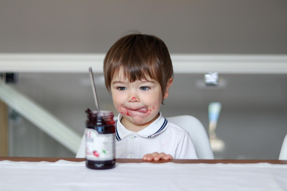 Child sitting at a table, with jelly jar in front of him and jelly smeared all over his face.