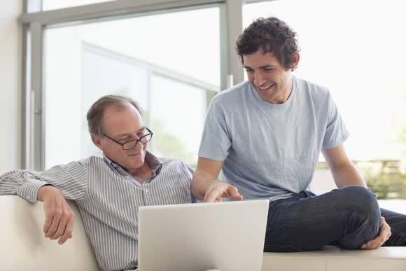 An older man and a younger man looking at something on a laptop.