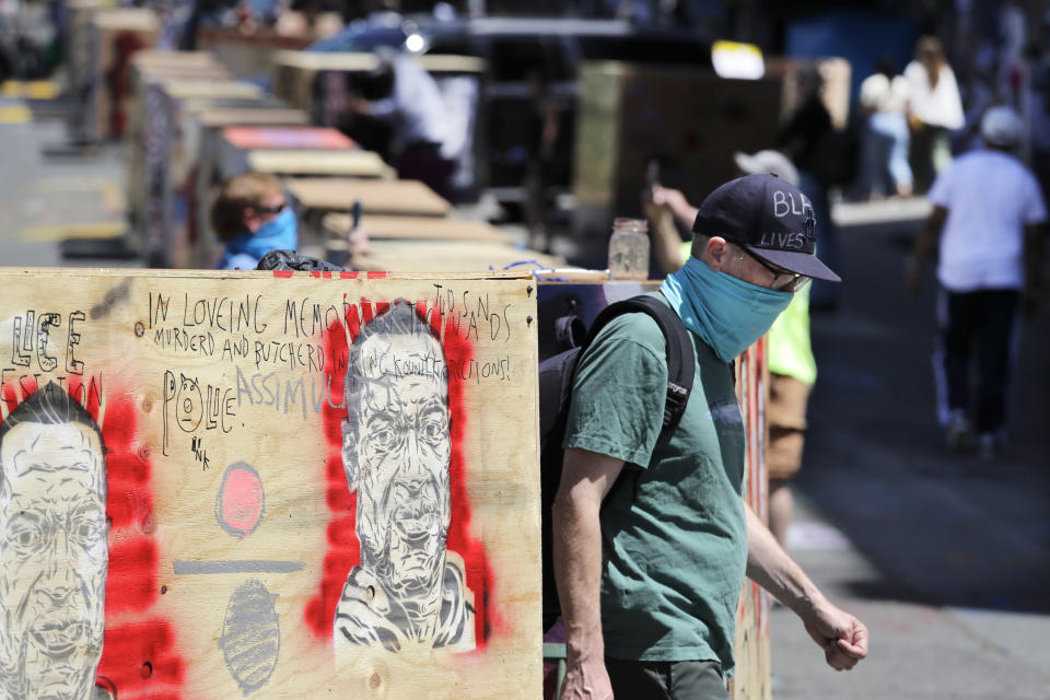 A man walks between barricades blocking a street adjacent to a closed police precinct Thursday, June 18, 2020, in Seattle, in what has been named the Capitol Hill Occupied Protest zone. Police pulled back from several blocks of the city's Capitol Hill neighborhood near the Police Department's East Precinct building earlier in the month after clashes with people protesting the death of George Floyd in Minneapolis. (AP Photo/Elaine Thompson)