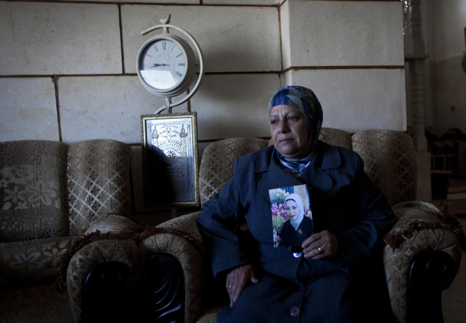 In this photo taken Saturday, Feb. 1, 2014, Palestinian Khadra al-Akhras poses with a photo of her late daughter Ayat al-Akhras, who blew herself up in a suicide bombing outside a Jerusalem supermarket in 2002, at the family house in the West Bank city of Bethlehem. More than a decade later, after appeals from human rights groups, Israel is handing over some 30 bodies of Palestinian assailants, including that of Ayat. (AP Photo/Nasser Nasser)