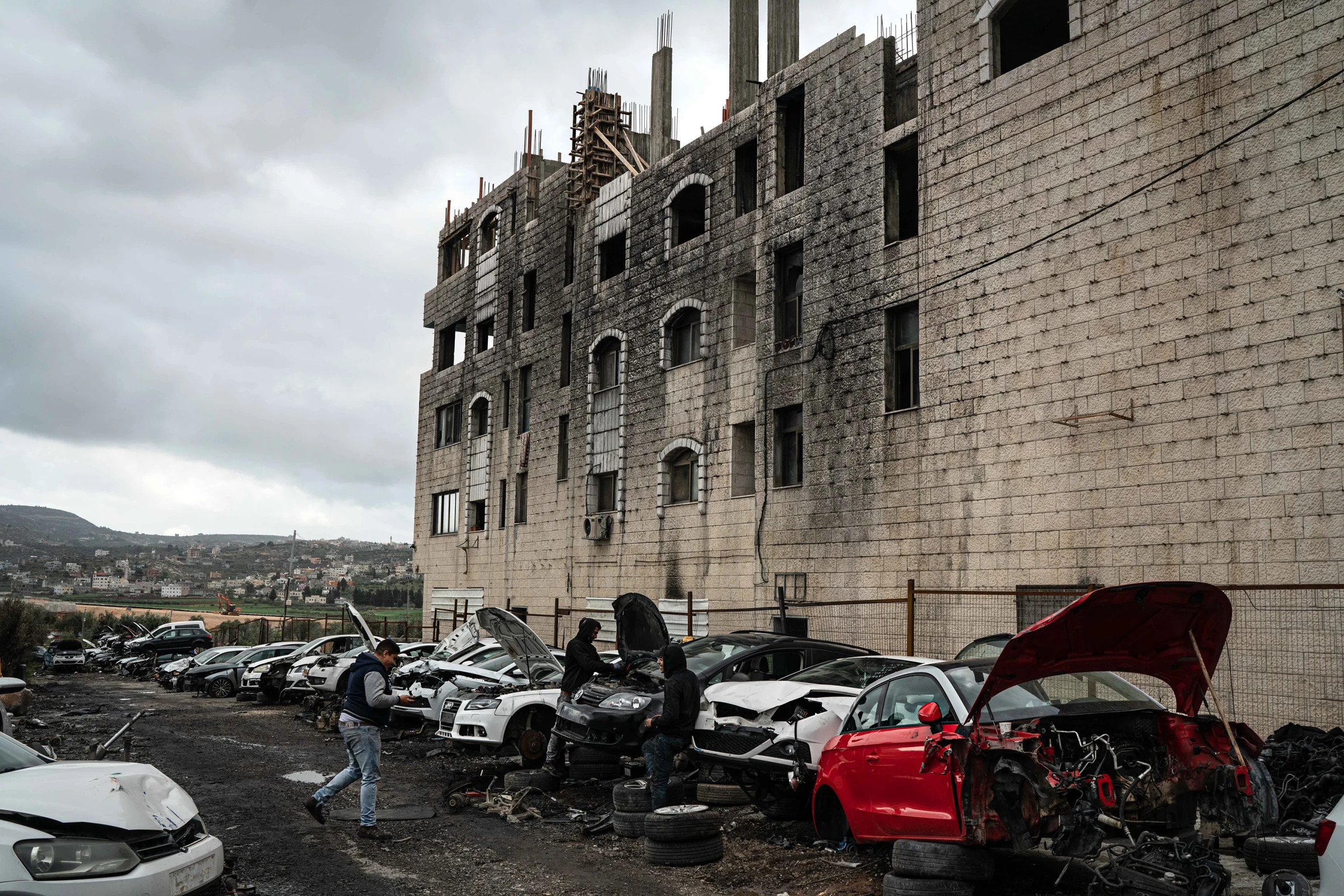 Palestinian men fix cars in the West Bank village of Huwara, March 15, 2023, that were set ablaze by Jewish settlers a few weeks earlier. (Samar Hazboun/The New York Times)