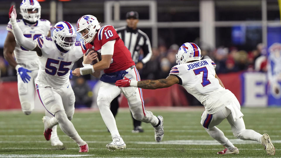 New England Patriots quarterback Mac Jones (10) runs between Buffalo Bills cornerback Taron Johnson (7) and defensive end Boogie Basham (55) during the first half of an NFL football game, Thursday, Dec. 1, 2022, in Foxborough, Mass. (AP Photo/Steven Senne)