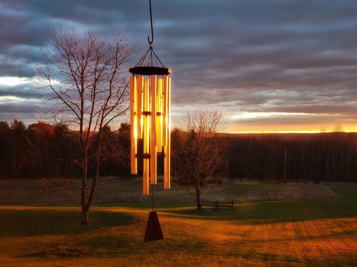 windchimes hanging in front of the rising sun which is starting to light the bare trees and ground in the background