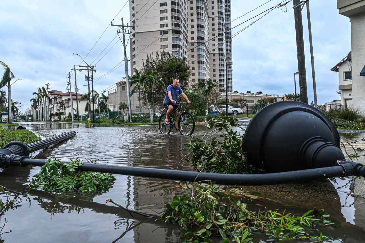 A man bikes through water past a downed street lamp.