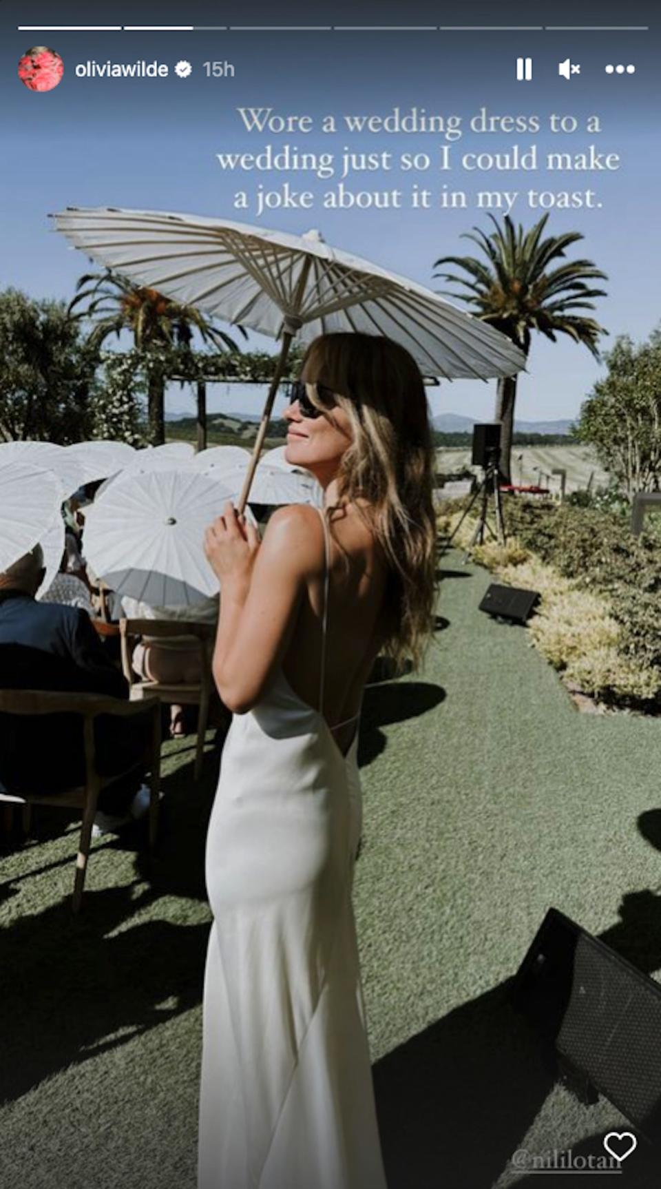 Olivia Wilde poses in a white dress holding a parasol.