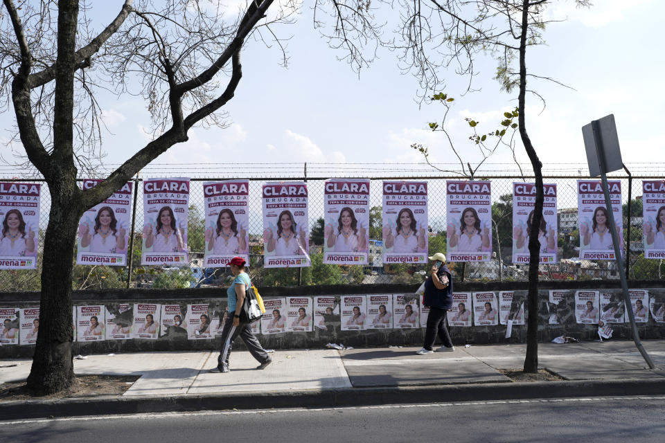 Dos personas pasan por delante de carteles electorales con la imagen de Clara Brugada, la candidata del partido gobernante en las elecciones municipales, en la Ciudad de México, el 25 de mayo de 2024. (AP Foto/Marco Ugarte)