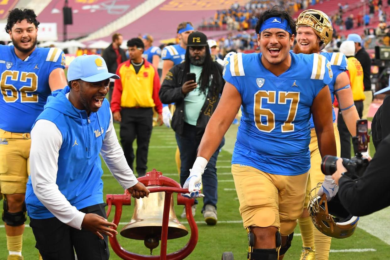 UCLA athletic director Martin Jarmond and offensive lineman Yutaka Mahe roll the victory bell off the Coliseum field