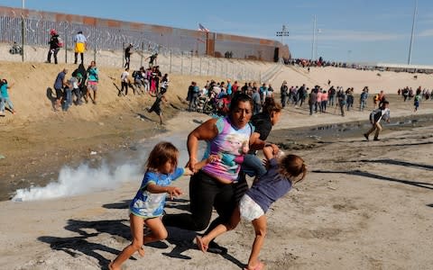 A migrant family, part of a caravan of thousands traveling from Central America to the United States, run away from tear gas in front of the border wall between the U.S. and Mexico in Tijuana, Mexico - Credit: Reuters