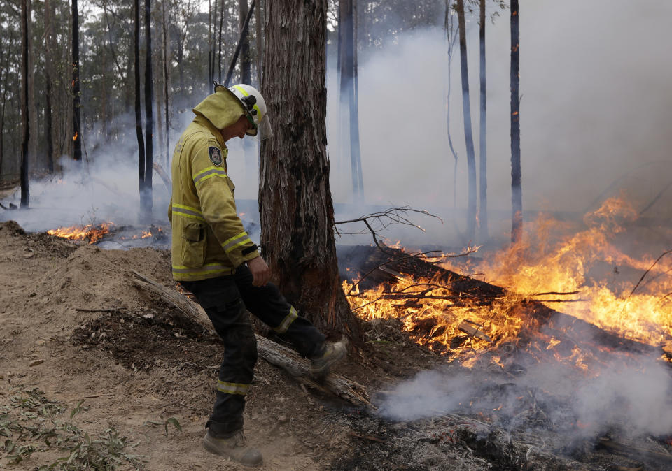 A firefighter kicks at a log while helping to build a containment line at a fire near Bodalla, Australia, Sunday, Jan. 12, 2020. Authorities are using relatively benign conditions forecast in southeast Australia for a week or more to consolidate containment lines around scores of fires that are likely to burn for weeks without heavy rainfall. (AP Photo/Rick Rycroft)