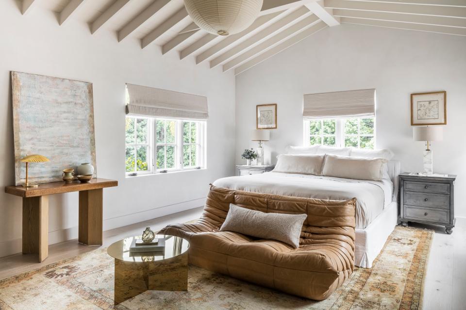 The primary bedroom inside Collarte Interiors’ Mediterranean Villa is equal parts sophisticated and soothing and features a vintage cognac Togo sofa from Ligne Roset, a Paul Frankl cork console, a brass origami-inspired Slit Coffee Table from Hay, and an Akari light sculpture overhead.