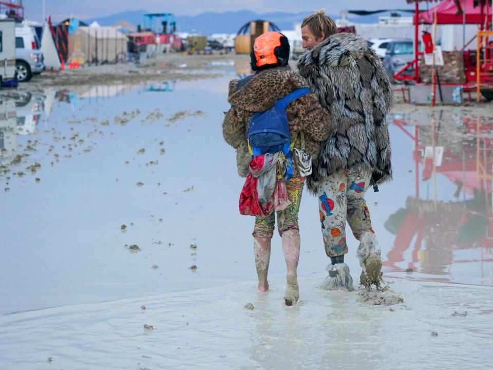 Two festival goers walking through the mud, arm-in-arm.