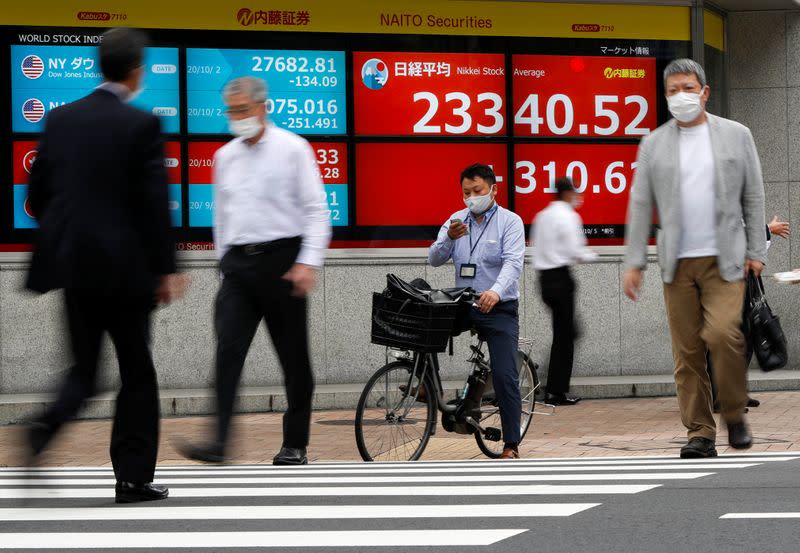 Passersby wearing protective face masks walk past a screen displaying Nikkei share average and world stock indexes, amid the coronavirus disease (COVID-19) outbreak, in Tokyo