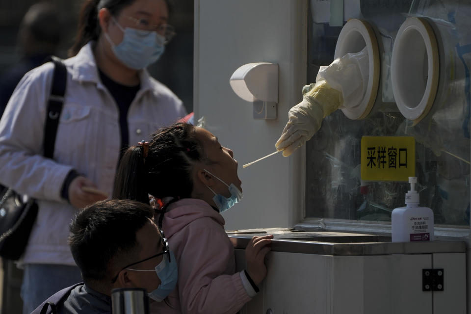 A man wearing a face mask helps a child to get her routine COVID-19 throat swab at a coronavirus testing site in Beijing, Thursday, Oct. 6, 2022. Sprawling Xinjiang is the latest Chinese region to be hit with sweeping COVID-19 travel restrictions, as China further ratchets up control measures ahead of a key Communist Party congress later this month. (AP Photo/Andy Wong)