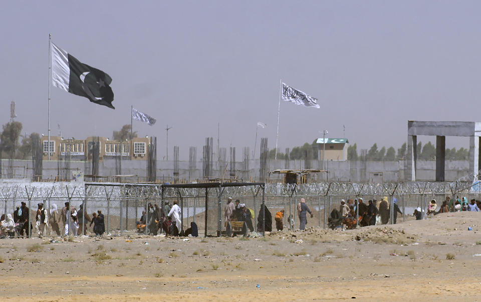 Pakistan and Taliban flags flutter on their respective sides while people walk through a security barrier to cross border at a border crossing point between Pakistan and Afghanistan, in Chaman, Pakistan, Wednesday, Aug. 18, 2021. Chaman is a key border crossing between Pakistan and Afghanistan, normally thousands of Afghans and Pakistanis cross daily and a steady stream of trucks passes through, taking goods to Afghanistan. (AP Photo/Jafar Khan)