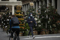 A man wearing a face mask walks past Christmas trees in Covent Garden, during England's second coronavirus lockdown in London, Thursday, Nov. 26, 2020. As Christmas approaches, most people in England will continue to face tight restrictions on socializing and business after a nationwide lockdown ends next week, the government announced Thursday. (AP Photo/Matt Dunham)