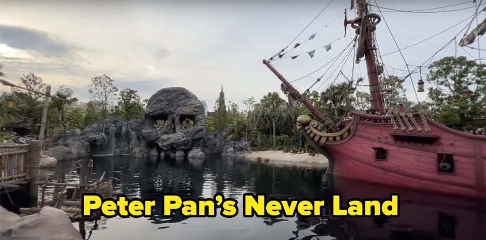 Skull-shaped rock formation and pirate ship docked in a scenic water setting surrounded by trees