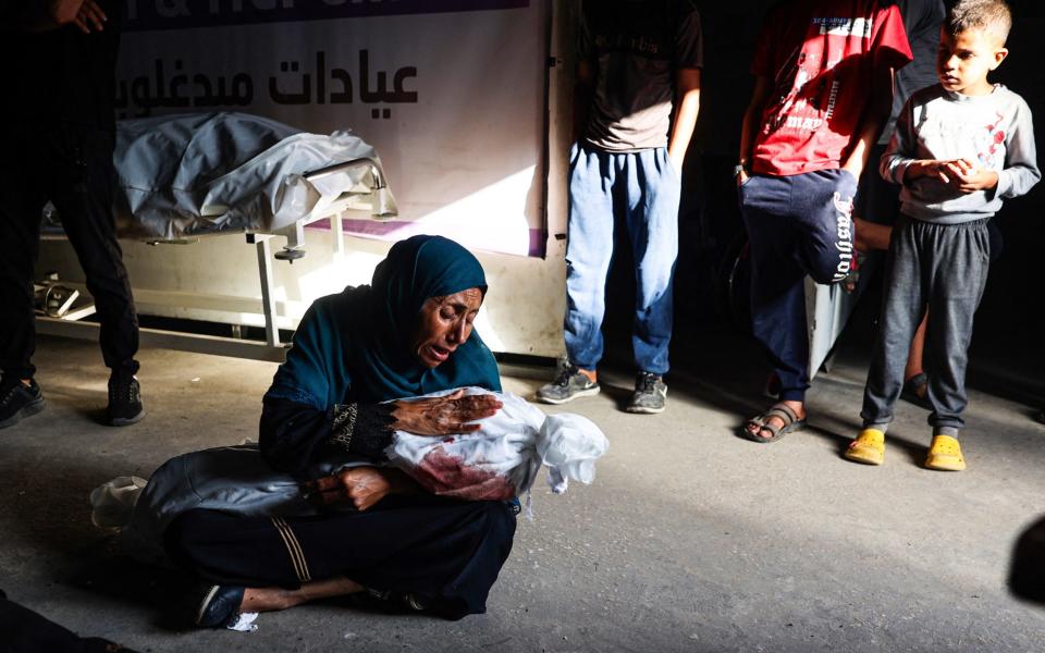 A child looks on as Palestinian woman holds the shrouded body of child killed in Israeli bombardment, at a health clinic in the area of Tel al-Sultan