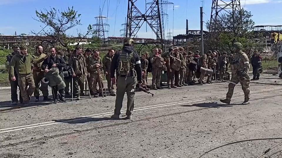 This screen grab obtained from a handout video taken on May 17, 2022 and released by the Russian Defence Ministry on May 18, 2022, shows Ukrainian service members as they line up on a road in front of pro-Russian military personnel after leaving the besieged Azovstal steel plan (Russian Defence Ministry/AFP via)