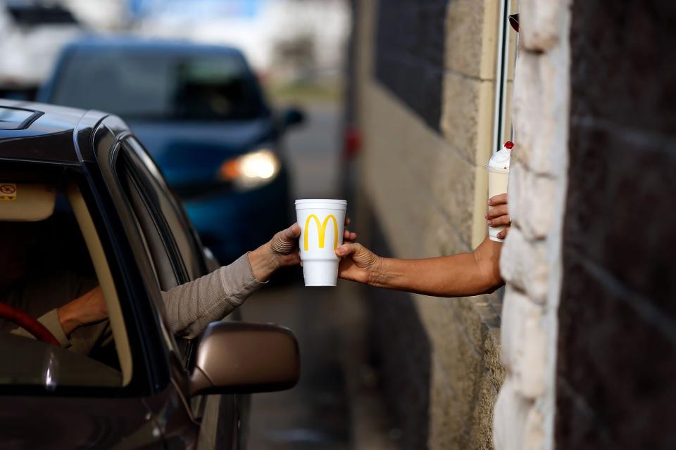 A worker passes a beverage to a customer at the drive-thru window at a McDonald's fast food restaurant