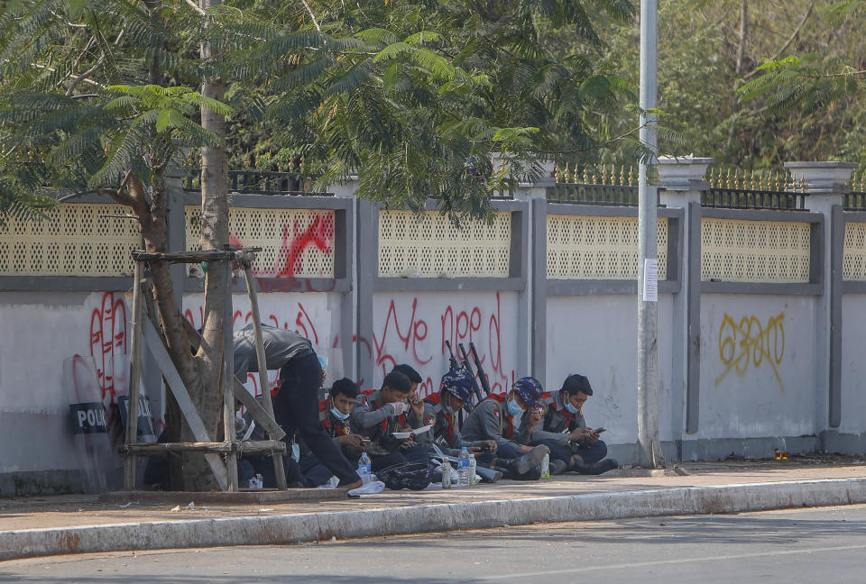 Police officers eat a meal along a sidewalk near a graffiti against the recent military coup in Mandalay, Myanmar, Friday, Feb. 12, 2021. Myanmar's coup leader used the country's Union Day holiday on Friday to call on people to work with the military if they want democracy, a request likely to be met with derision by protesters who are pushing for the release from detention of their country's elected leaders. (AP Photo)