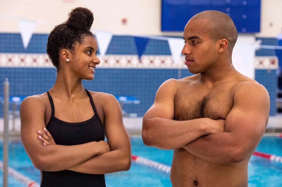 Swimmers Jayla and Troy Pina smile at each other with their arms crossed, a swimming pool in the background