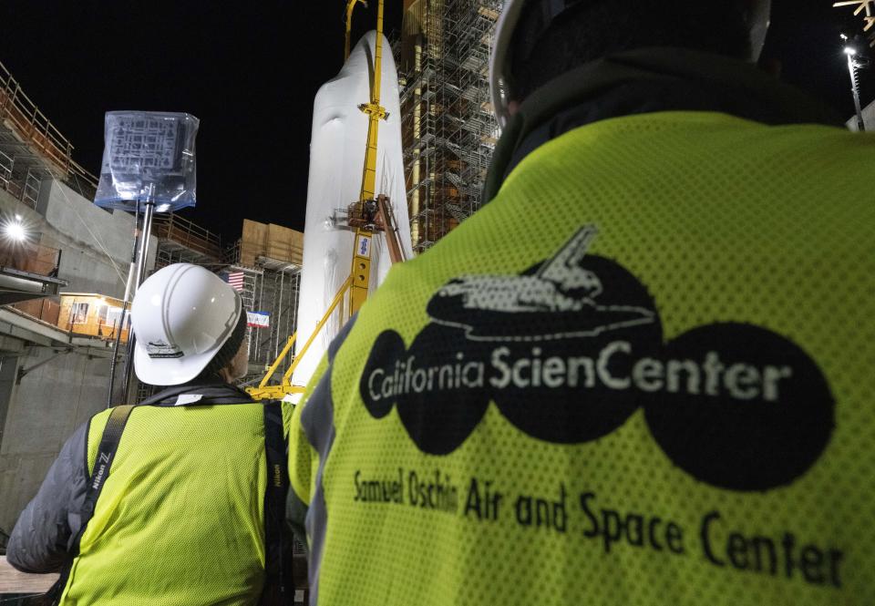 People looks at the Space Shuttle Endeavour at the site of the future Samuel Oschin Air and Space Center on Tuesday, Jan. 30, 2024, in Los Angeles. NASA's retired Space Shuttle Endeavour was carefully hoisted late Monday to be mated to a huge external fuel tank and its two solid rocket boosters at a Los Angeles museum where it will be uniquely displayed as if it is about to blast off. (AP Photo/Richard Vogel)