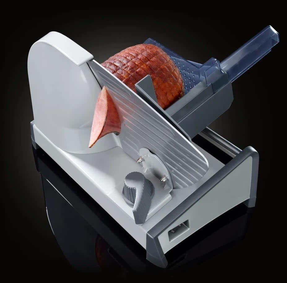 Slicing machine with a piece of ham, blade midway through a slice