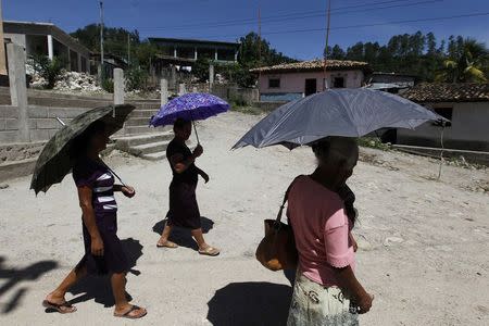 Women, whose relatives work in the U.S., use umbrellas to shield from the sun as they walk in the small villa ge of El Guantillo, outskirts of Tegucigalpa June 25, 2014. REUTERS/Jorge Cabrera