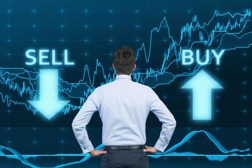 man standing in front of large stock chart with sell and buy arrows