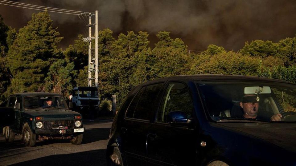 People drive as smoke rises from a wildfire burning in the village of Varnavas, near Athens, Greece, August 11, 2024