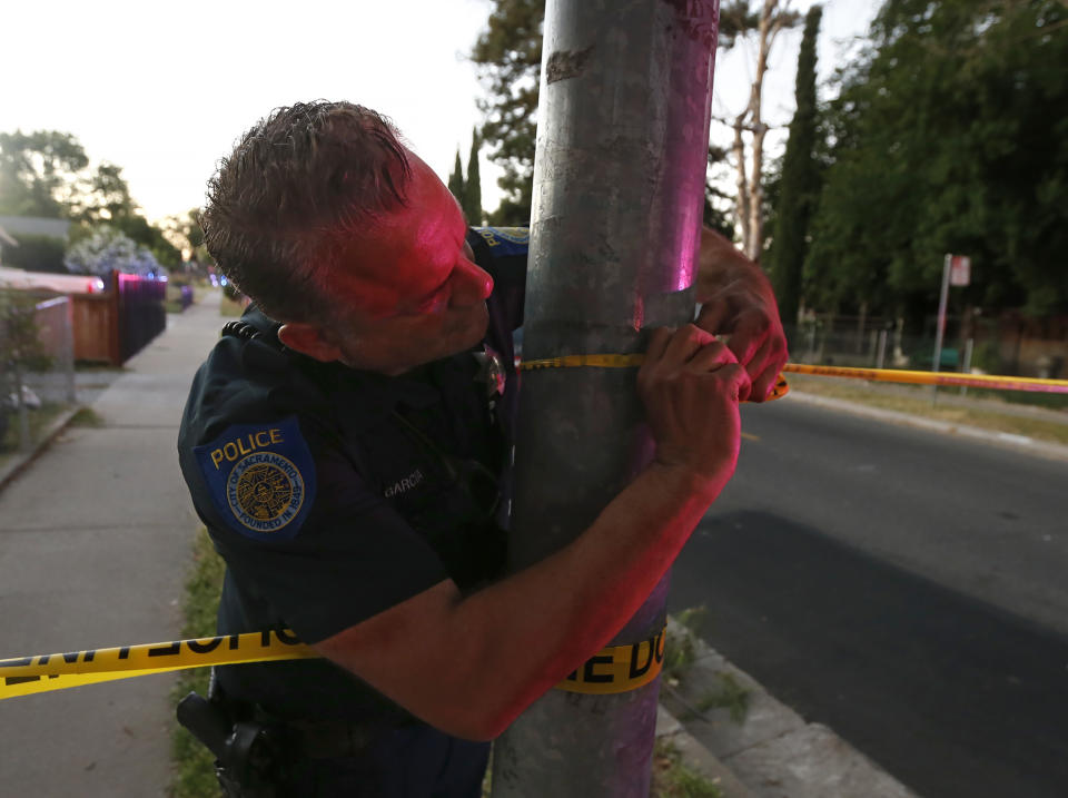 A Sacramento Police officer puts up crime scene tape near a home that authorities have surrounded where a gunman has taken refuge after shooting a Sacramento police officer, Wednesday, June 19, 2019, in Sacramento, Calif. (AP Photo/Rich Pedroncelli)