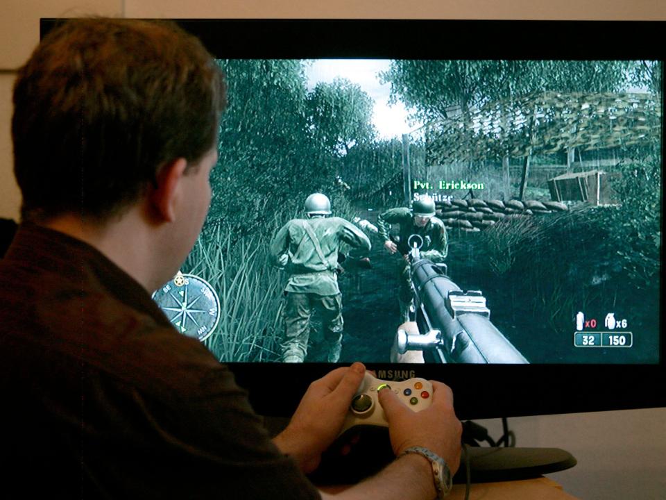 A man holds a video game controller while playing Call of Duty 3 as seen on a screen in 2006.
