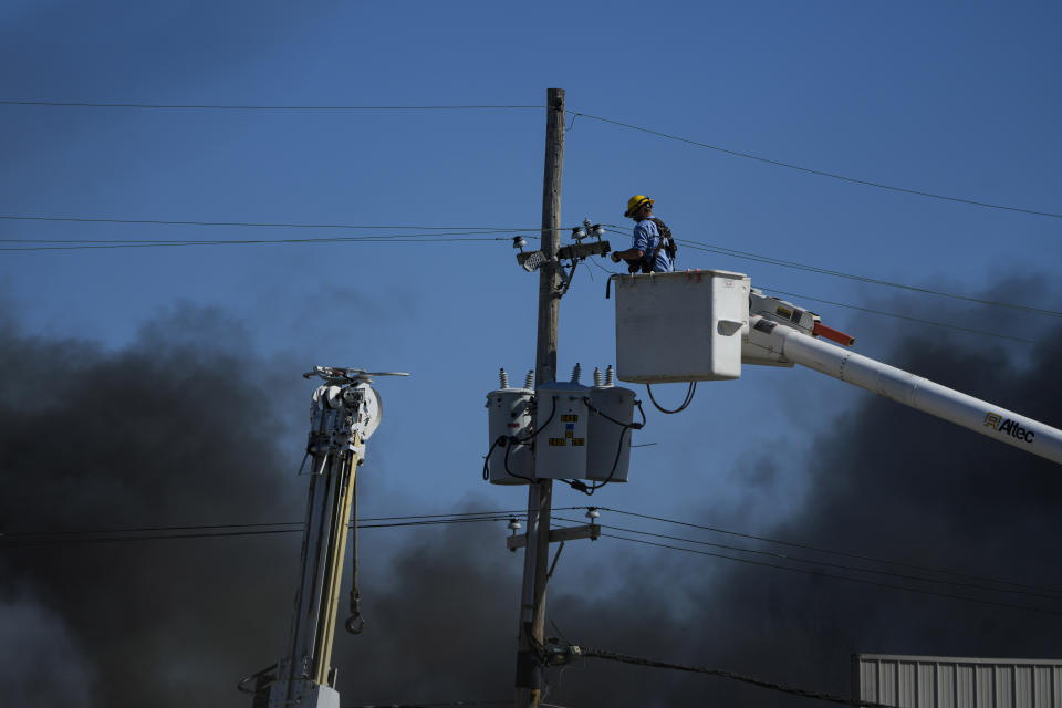 Utility workers remove utilities from the area as smoke billows from an industrial fire in Richmond, Ind., Wednesday, April 12, 2023. Authorities urged people to evacuate if they live near the fire. The former factory site was used to store plastics and other materials for recycling or resale. (AP Photo/Michael Conroy)