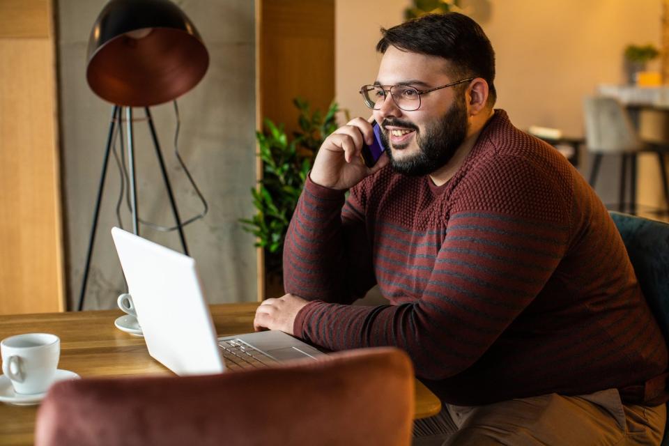 An investor smiles while talking on the phone in front of a laptop.