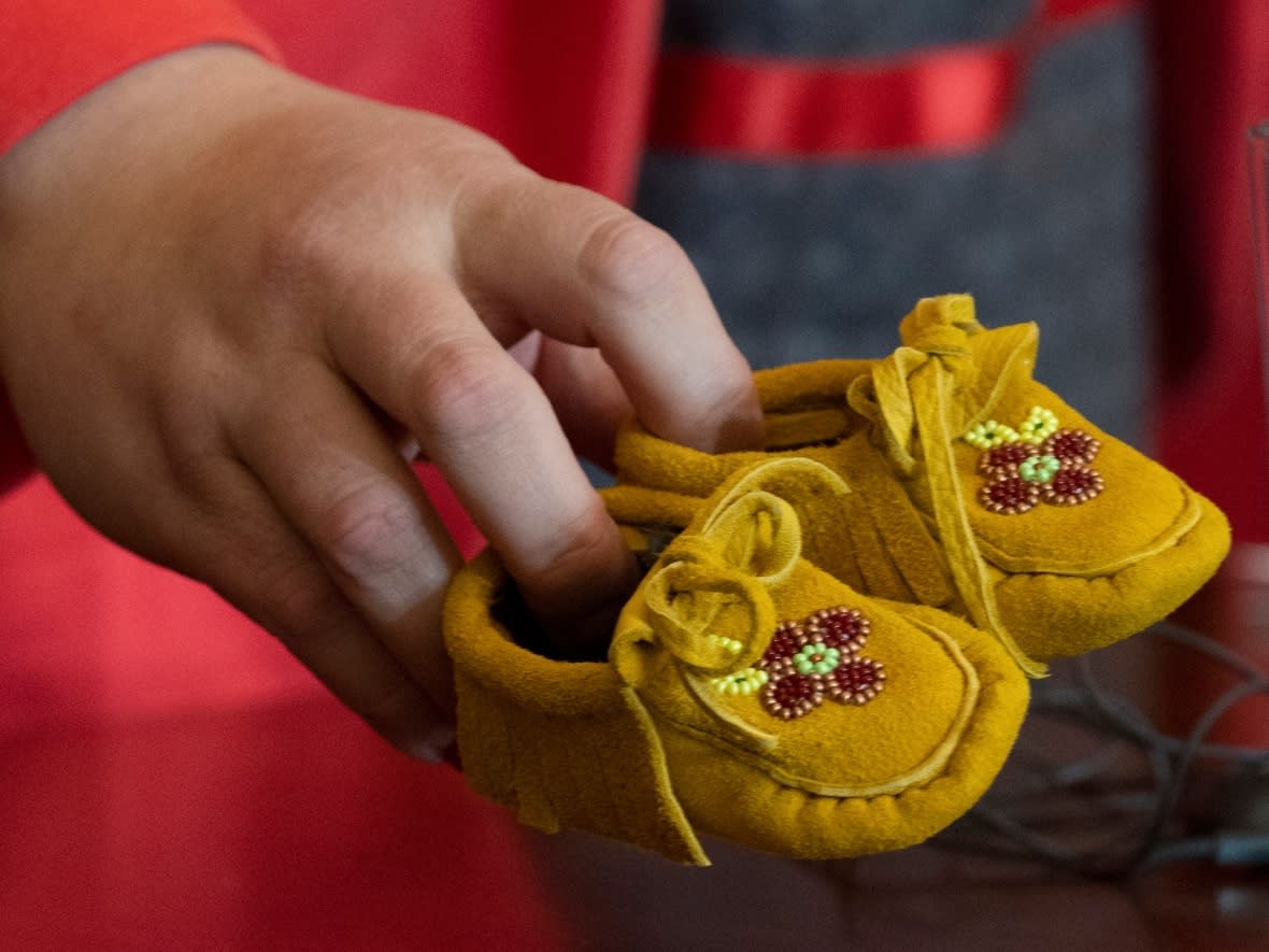 Manitoba Regional Chief Cindy Woodhouse picks up a pair of children’s moccasins she placed on her desk in January 2022 following announcement of the since-scuttled $20-billion child-welfare settlement agreement. (Adrian Wyld/The Canadian Press - image credit)