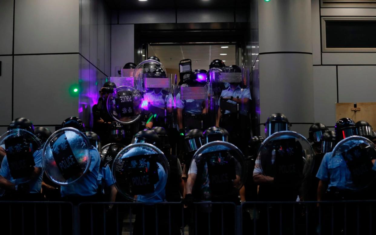 Police officers armed with riots gear stand outside Mong Kok police station during pro-democracy protesters march in Hong Kong on Saturday - AP