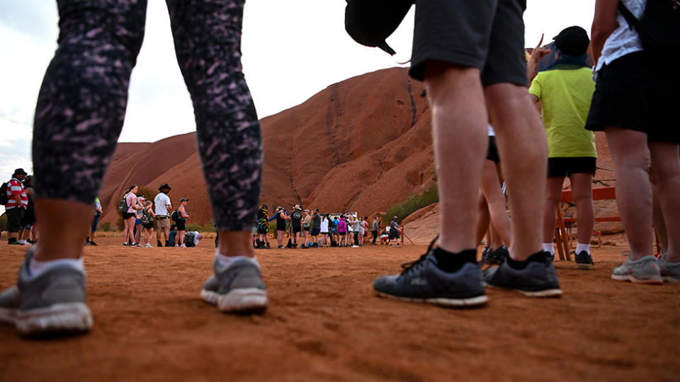 Picture of tourists standing around Uluru, ready to climb, before the climbing ban in enforced.