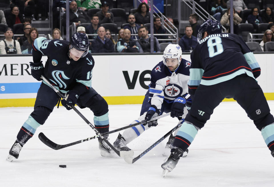 Winnipeg Jets defenseman Dylan DeMelo (2) shoots between Seattle Kraken left wing Jared McCann (19) and defenseman Brian Dumoulin (8) with the shot blocked during the second period of an NHL hockey game, Friday, March 8, 2024, in Seattle. (AP Photo/John Froschauer)