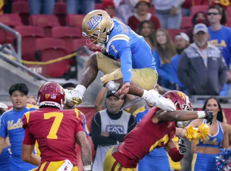 Los Angeles, CA - November 20: UCLA quarterback Dorian Thompson-Robinson hurdles high over USC safety Chase Williams, left, and cornerback Isaac Taylor-Stuart as he scores a touchdown on the play in the fourth quarter at Los Angeles Memorial Coliseum in Los Angeles on Saturday, Nov. 20, 2021. UCLA beat USC 62-33. (Allen J. Schaben / Los Angeles Times)