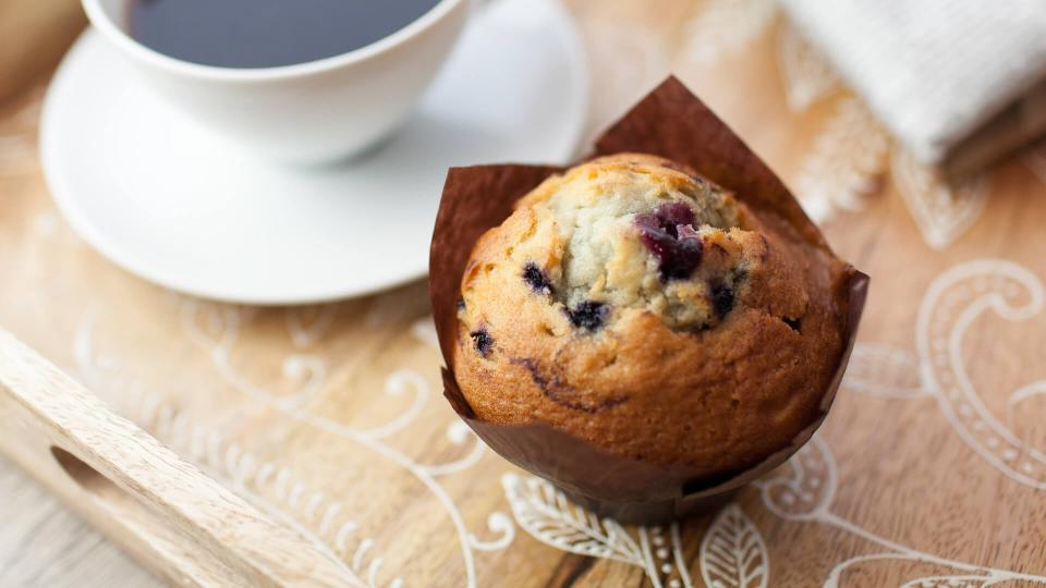 Black coffee in a cup and saucer with a blueberry muffin on a wooden tray with newspaper.