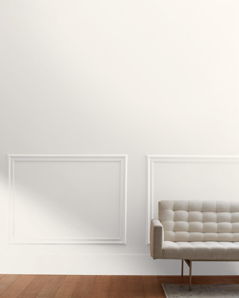A minimal room with a paneled wall painted in Atrium White by Benjamin Moore, in front of which sits a white couch.