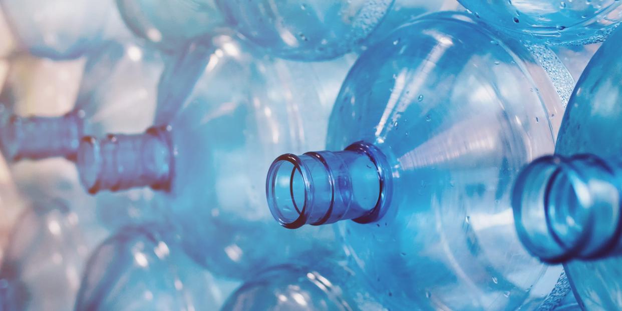 Empty bottles are stacked in a row. Cleaning of plastics in the production of pure water. Background from blue bottles with backlight. Environmental problem due to plastic in everyday life