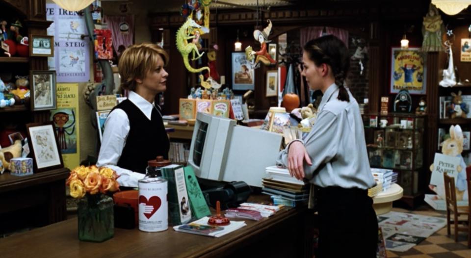 Meg Ryan standing at the register inside her character's book shop in "You've Got Mail" speaking to co-star Parker Posey.