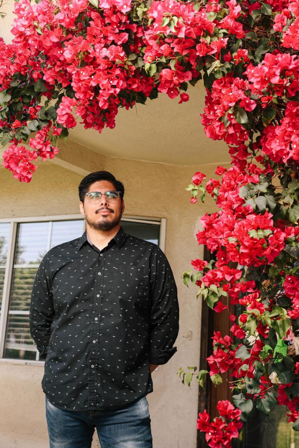 A bearded man in glasses and a black shirt poses amid red blossoms.