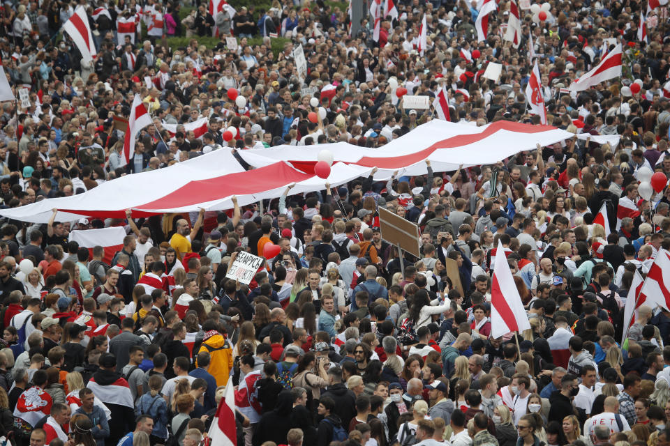 Protesters unveil historical flag of Belarus as thousands of people gather for a protest at the Independence square in Minsk, Belarus, Sunday, Aug. 23, 2020. Demonstrators are taking to the streets of the Belarusian capital and other cities, keeping up their push for the resignation of the nation's authoritarian leader. President Alexander Lukashenko has extended his 26-year rule in a vote the opposition saw as rigged. (AP Photo/Dmitri Lovetsky)