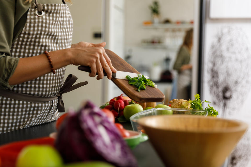 Person slicing herbs in kitchen with various vegetables on countertop